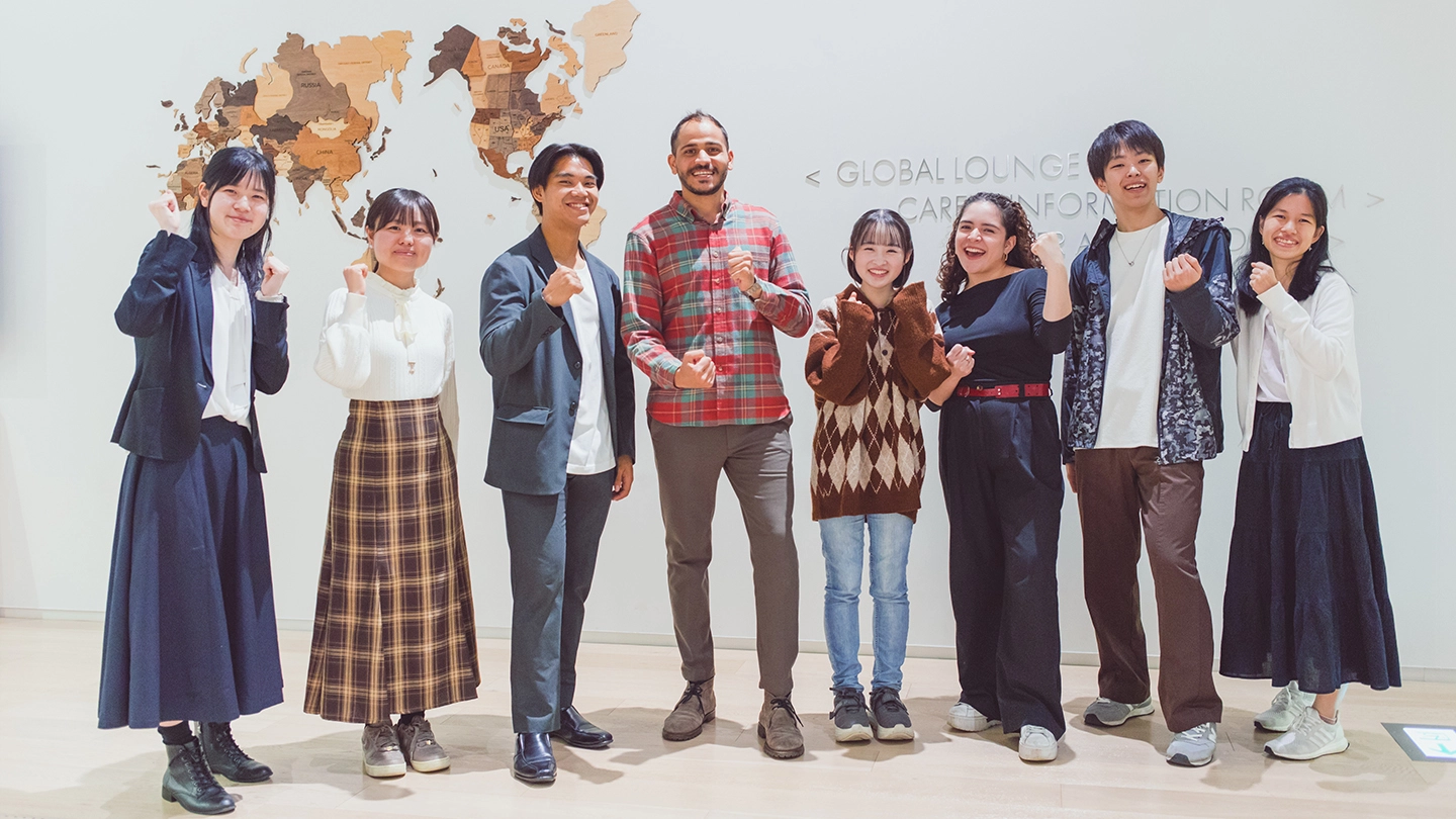 A group of students and faculty members posing for a commemorative photo in front of a world map.