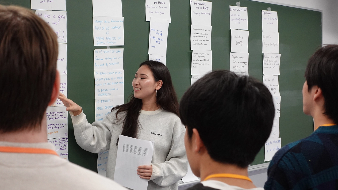 A scene inside the classroom showing the presenter explaining while pointing to numerous notes posted on the blackboard.